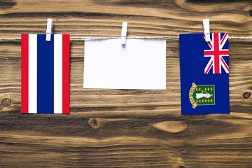 Hanging flags of Thailand and British Virgin Islands attached to rope with clothes pins with copy space on white note paper on wooden background.Diplomatic relations between countries.