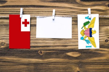 Hanging flags of Tonga and United States Virgin Islands attached to rope with clothes pins with copy space on white note paper on wooden background.Diplomatic relations between countries.