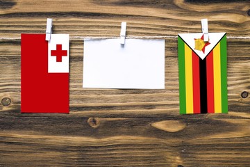 Hanging flags of Tonga and Zimbabwe attached to rope with clothes pins with copy space on white note paper on wooden background.Diplomatic relations between countries.