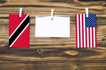 Hanging flags of Trinidad And Tobago and United States attached to rope with clothes pins with copy space on white note paper on wooden background.Diplomatic relations between countries.