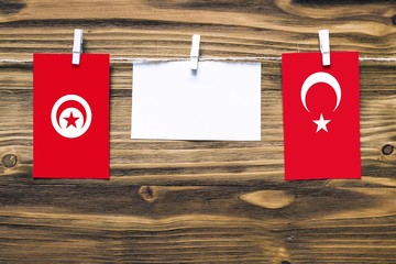 Hanging flags of Tunisia and Turkey attached to rope with clothes pins with copy space on white note paper on wooden background.Diplomatic relations between countries.