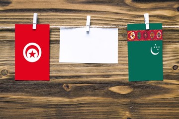 Hanging flags of Tunisia and Turkmenistan attached to rope with clothes pins with copy space on white note paper on wooden background.Diplomatic relations between countries.