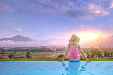 Women sitting at the pool looking at the sunrise in the morning.Women are relaxing at the poolside.Relaxing Holidays in Summer.