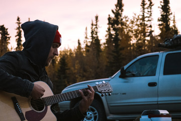 Young man with denim jacket playing guitar in Alaska nature during autumn season and sunset - 300053499