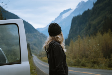 Young blonde woman in beanie smiling and standing next to the highway in Alaskan valley