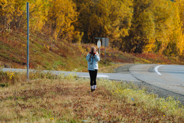 Young blonde woman in denim jacket photographing nature during autumn season