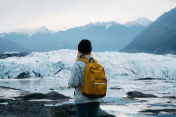 Young woman in denim jacket and backpack walking on glacier in Alaska