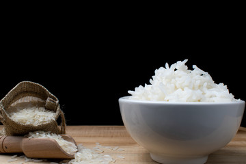 White ceramic cup with cooked rice Resting on a wooden table with a bag of rice grains and a wooden spoon, with a black backdrop.