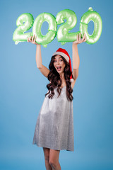 woman holding 2020 new year balloons wearing santa hat and dress