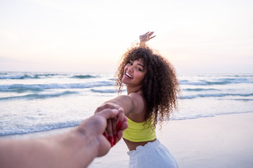 Girl holding male hand and running on tropical exotic beach to the ocean. Follow me shot of young woman pull her boyfriend on the sea shore. Summer vacation or holiday. POV. - obrazy, fototapety, plakaty