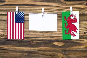 Hanging flags of United States and Wales attached to rope with clothes pins with copy space on white note paper on wooden background.Diplomatic relations between countries.