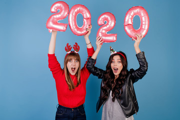 women with 2020 new year balloons wearing funny christmas hoops isolated over blue