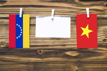 Hanging flags of Venezuela and Vietnam attached to rope with clothes pins with copy space on white note paper on wooden background.Diplomatic relations between countries.