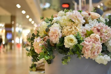 A bouquet of flowers in a shopping center against the background of blurry lights and shop windows.