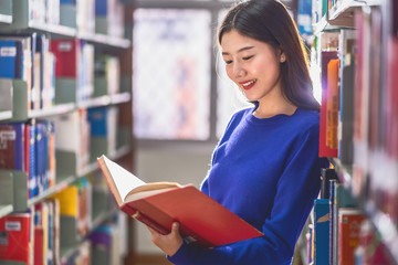 Asian young Student in casual suit standing and reading the book at book shelf in library of university or colleage with various book background, Back to school concept
