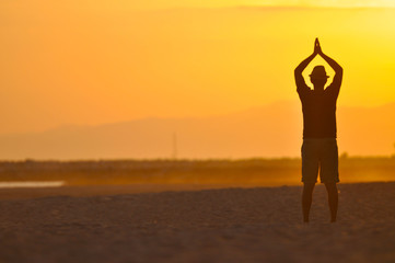 Man on the beach meditating at sunset.
