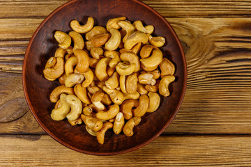 Ceramic plate with roasted cashew nuts on a wooden table. Top view