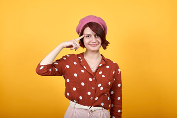 Pretty young caucasian woman wearing red shirt with white polka dot looking funny and happy making suicide gesture, tired of everything. Shoots with his hand imitating gun