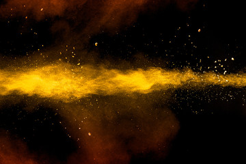 Abstract yellow orange powder explosion on black background.Freeze motion of yellow  orange dust particles splash.