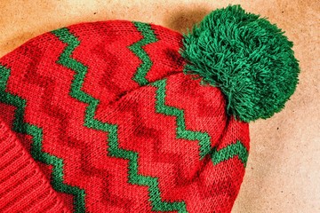 Knitted red hat with green ornament on a wooden background
