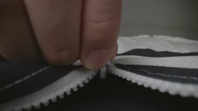 Extreme close up zipper with hand unzipping the sweater jacket zipper while camera following the man hand. Fashion, textile and clothing industry concept.