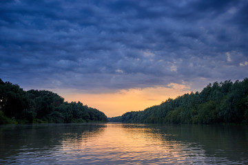 Obraz na płótnie Canvas Beautiful bright dramatic sunset over Danube river with forest along riverside