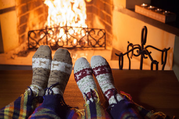 Man and woman in warm knitted socks with cups of hot punch in front of the fireplace