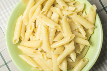 Tubular pasta in green plate on kitchen table.