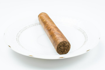 Thick cigar from twisted sheets on white saucer with white background.