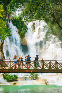 Tourists take pictures and selfies on a bridge with the Kuang Si Water Falls in the background close to Luang Prabang, Laos.