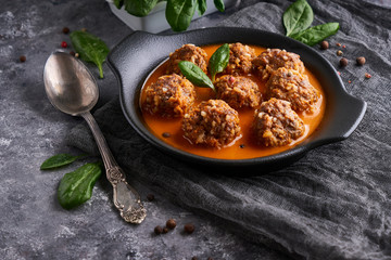 Appetizing homemade meatballs with tomato sauce and spinach in a plate on a dark background