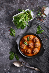 homemade meatballs with tomato sauce and spinach served in a plate on a dark stone table Top view