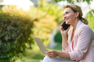 Close-up portrait of a smiling woman calling by phone on the street.  Happy businesswoman is using...