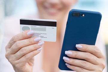 Businesswoman with a credit card and phone makes purchasing outdoors. Successful  woman is using smart phone and bank card for online shopping. Beautiful smiling white woman holds card and cell phone