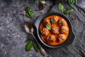 Appetizing homemade meatballs with tomato sauce and spinach served in a plate on a dark stone table...