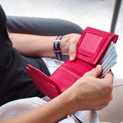 Midsection of the young woman paying bill in the restaurant. Red wallet with dollars