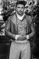 Portrait of handsome gentleman dressed in vintage costume standing in stately home courtyard with railings in background