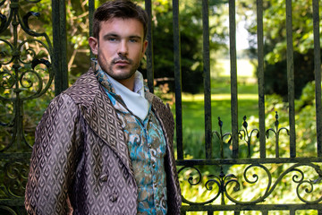 Portrait of handsome gentleman dressed in vintage costume standing in stately home courtyard with...