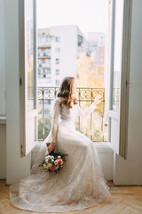 Stylish wedding in European style. Beautiful bride sitting on a panoramic window.