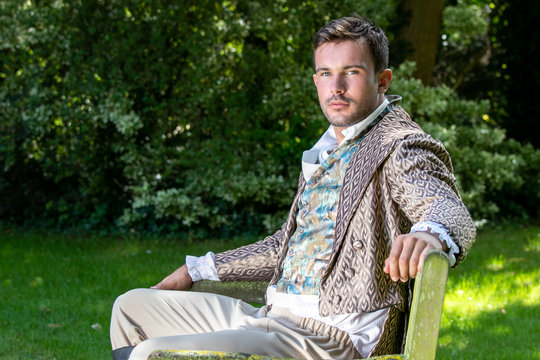Portrait of handsome gentleman dressed in vintage costume, sitting on garden bench, looking at camera