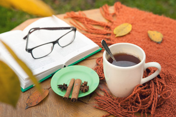 A book, glasses and a cup on the table in the garden. Autumn. Tea. Coffee.