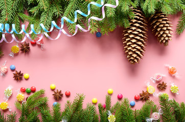 Flat lay design of Christmas greeting card of fir twigs cones, paper streamer, candies and spices on pink background. Space for text