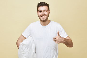 Studio image of cheerful overjoyed young Caucasian man in white t-shirt looking at camera with...