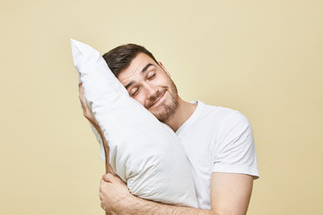 Horizontal image of handsome cute young man with bristle posing with head on white soft pillow...