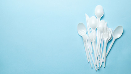 Plastic cutlery, forks, spoons and knives. Pollution of the environment with plastic and microplastics. Blue background. Copy space for text.