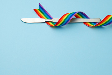 Scalpel and rainbow LGBT ribbon pride symbol. Sex change operation. Blue background. Copy space for text.