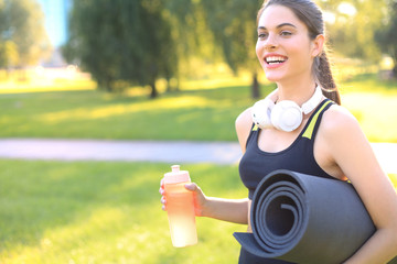 Beautiful happy young sports woman holding fitness rug in urban park.