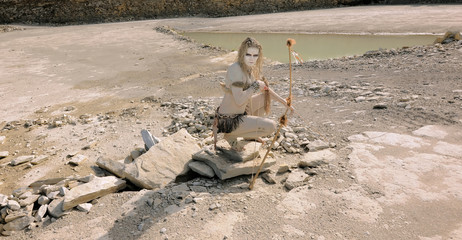 Fototapeta na wymiar A young woman is dressed as a prehistoric warrior. She is covered with mud, filth and dirt and is seen in a stone quarry area.