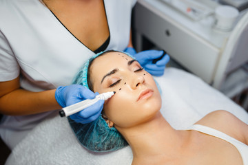 Cosmetician with marker puts dotted lines on face