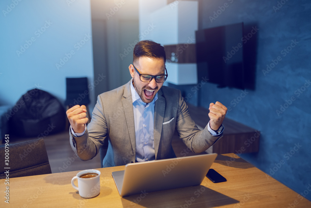 Wall mural handsome caucasian man in suit is excited for financial growth. living room interior.